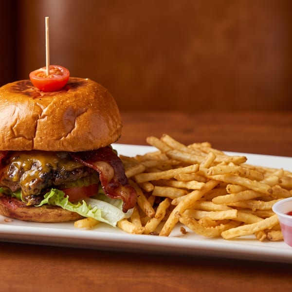 A bacon cheeseburger with lettuce, tomato, and a side of french fries with ketchup on a white plate.